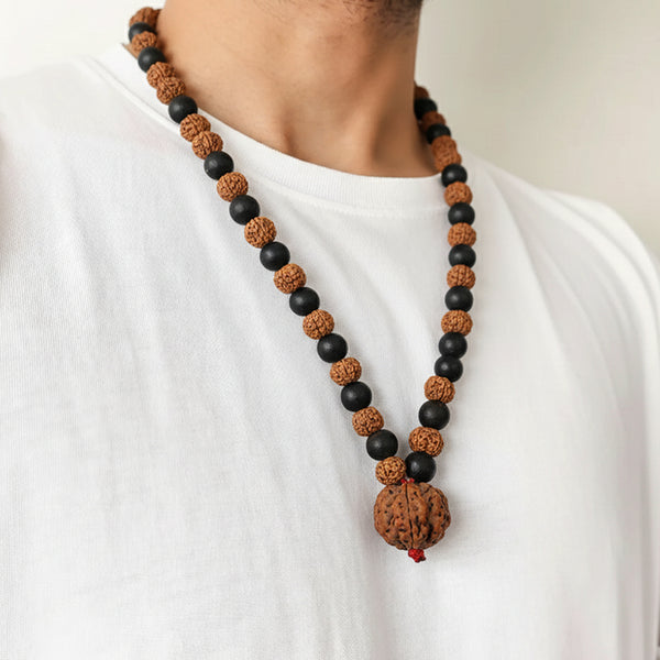 A man wearing an alternating black Karungali wood and brown Rudraksha bead mala necklace over a white t-shirt.