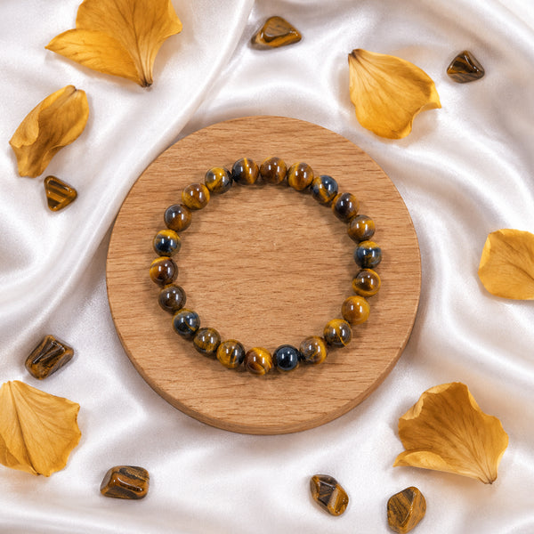 High-quality 8mm Tiger's Eye beads on a handcrafted spiritual bracelet displayed with tumbled stones and petals.