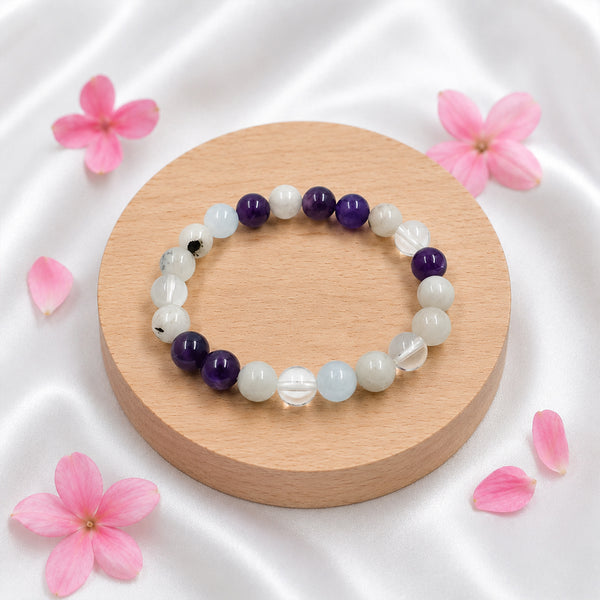 Overhead view of the Chandrashtama crystal bracelet with moonstone, amethyst, and clear quartz on a round wooden display.