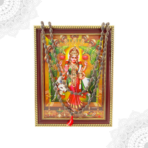 A colorful framed artwork depicting the goddess Vastu Grihalakshmi with a lotus bead malai hanging below.