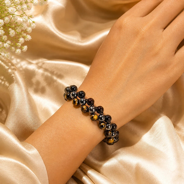 A close-up lifestyle shot showcasing the fit and texture of the handcrafted triple protection crystal bracelet on a person's wrist against a golden silk background.